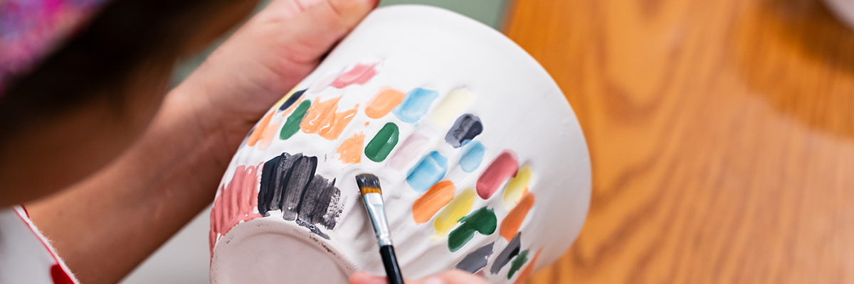 Pottery class student painting a piece of pottery with bright colors