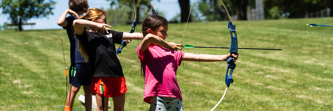 Three kids attempt to hit a target with a bow and arrow as they practice archery